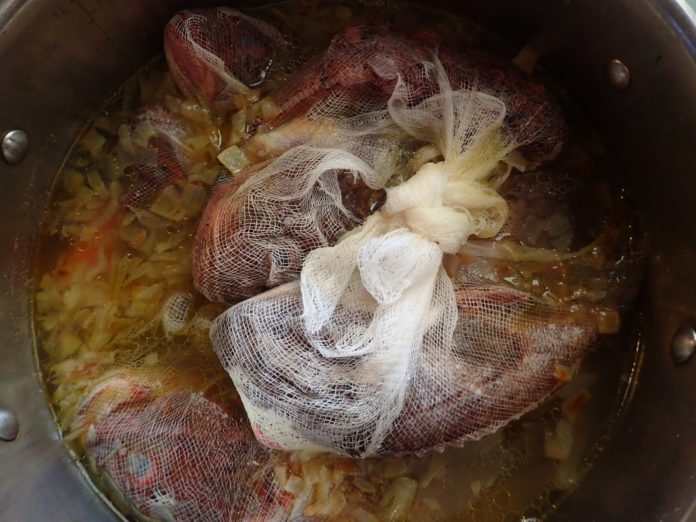 Fresh fish in cheesecloth simmers in apot of Greek fish soup - psarosoupa