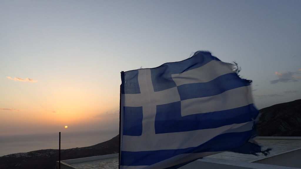 A Greek flag flying in the wind at sunset, high above the sea in Kasos