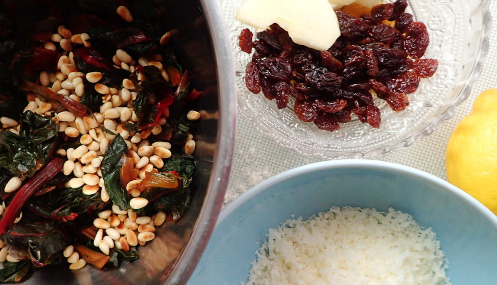 Filling ingredients for a Swiss chard tart - raisins, chard with pine nuts, and grated Parmesan cheese, in bowls